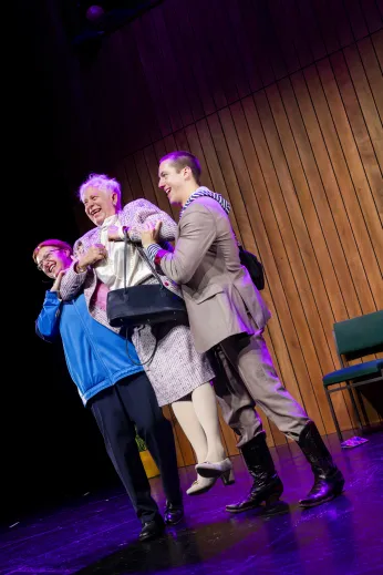 Szenenfoto "Mutti, was machst du da?" mit drei Personen nebeneinander, die Personen links und rechts heben die mittlere Person hoch