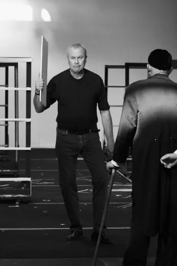 Schwarz-Weiß-Foto einer Person mit einer weißen Tafel in der Hand, davor eine weitere Person von hinten