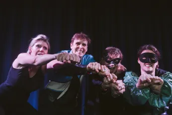 Vier Personen vor einem schwarzen Vorhang strecken ihre Hände in die Kamera.