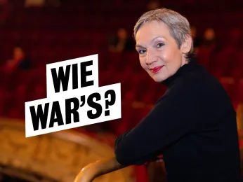 Portrait der Moderatorin Marion Brasch im ersten Rang des Großen Hauses. Sie lehnt an der Rangbrüstung, trägt einen schwarzen Rollkragenpullover und schaut über die linke Schulter direkt in die Kamera.