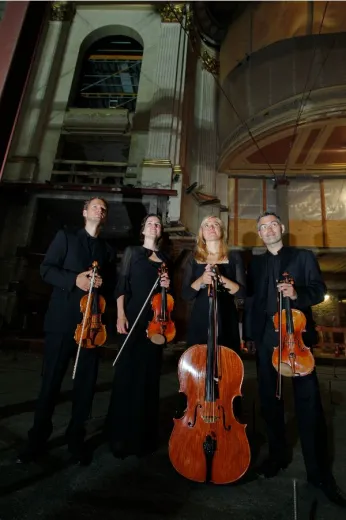 Das Bild ist aus der Froschperspektive aufgenommen und zeigt das Streichquartett mit seinen Instrumenten in einem verzierten Saal. 