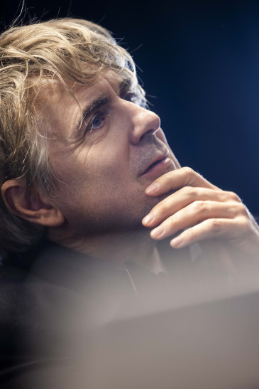 Portrait von Jens Harzer im Spiel. Es ist eine Nahaufnahme, er hält eine Hand ans Kinn, im unteren Bildteil ist ein atmosphärischer Störer zu erkennen. 