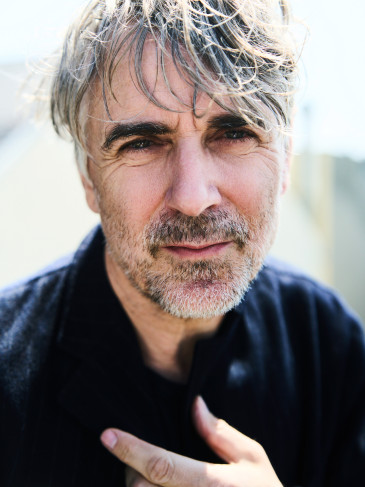 Schauspieler Jens Harzer im Profil, er schaut in die Kamera, hat eine Hand an der Brust.