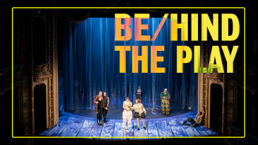 Ein Foto vom Bühnenportal, blaues Licht, vor einem beleuchteten Plastikvorhang sind einige Figuren in aufwändigen Kostümen zu erkennen. 