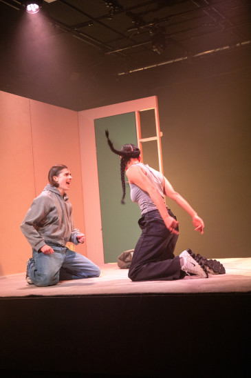 Amal Keller und Amelie Willberg auf dem Boden eines Wohnzimmers (Bühnenbild). Sie bewegen sich, Amal ist mit dem Rücken zum Publikum.