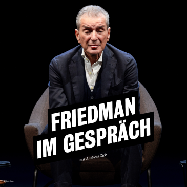 Michel Friedman sitzt auf einem dunklen Sessel vor dunklem Hintergrund. Er trägt einen dunklen Anzug über einem weißen Hemd und schaut, die Arme auf die Knie lehnend, direkt in die Kamera. 