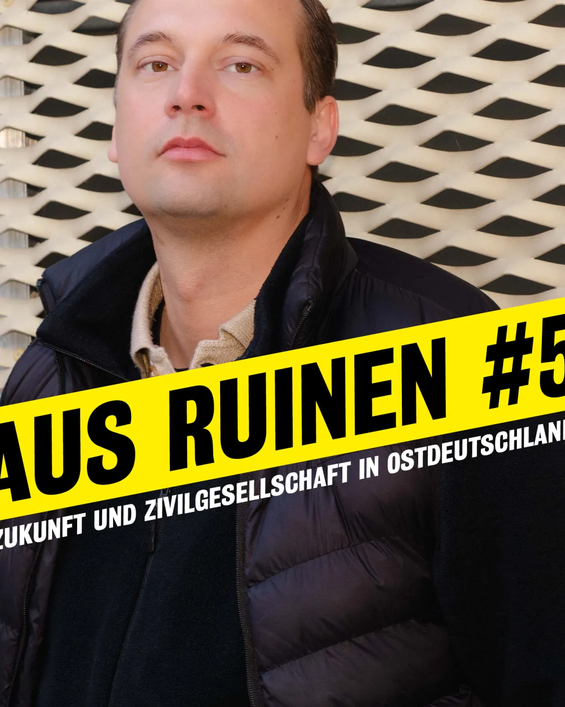 Autor und Host Hendrik Bolz lehnt an der Aussenwand des Neuen Hauses, er legt den Kopf etwas in den Nacken und schaut herausfordernd in die Kamera. 
