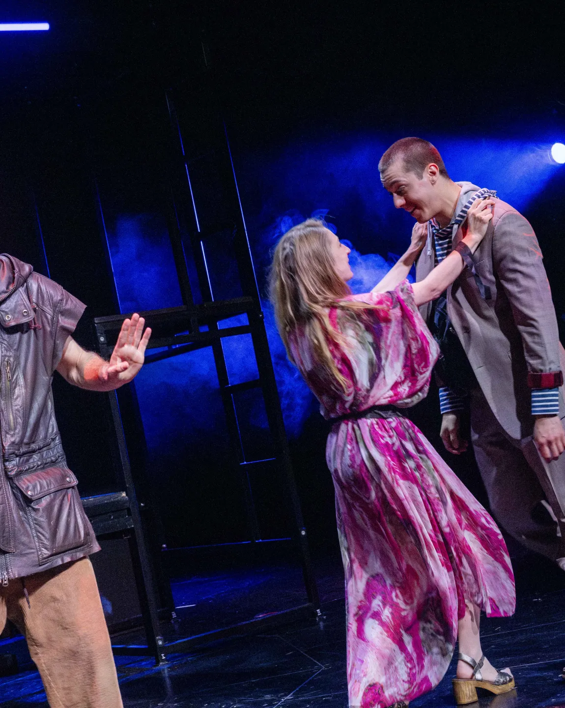 Szenenfoto "Mutti, was machst du da?" mit zwei Personen, die sich glücklich anschauen, dritte Person in Lederoberteil steht schulterzuckend daneben