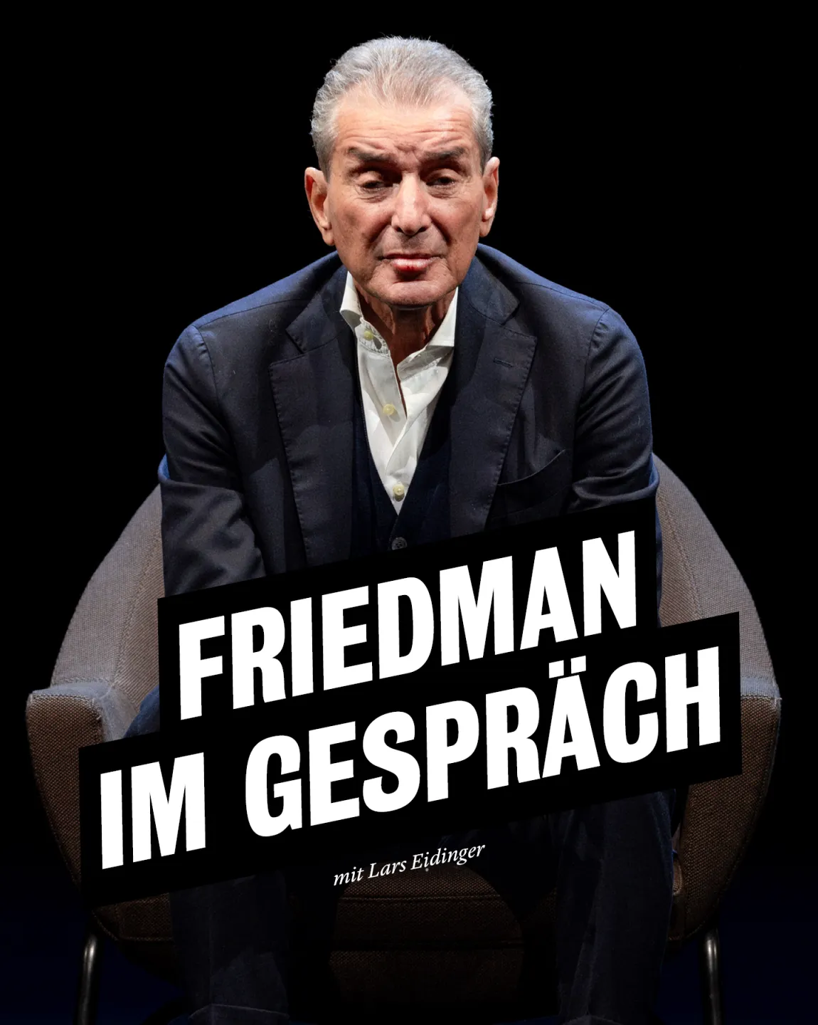 Portraitfoto von Michel Friedman. Er sitzt auf einem Sessel vor dunklem Hintergrund, trägt einen dunklen Anzug und schaut direkt in die Kamera. 