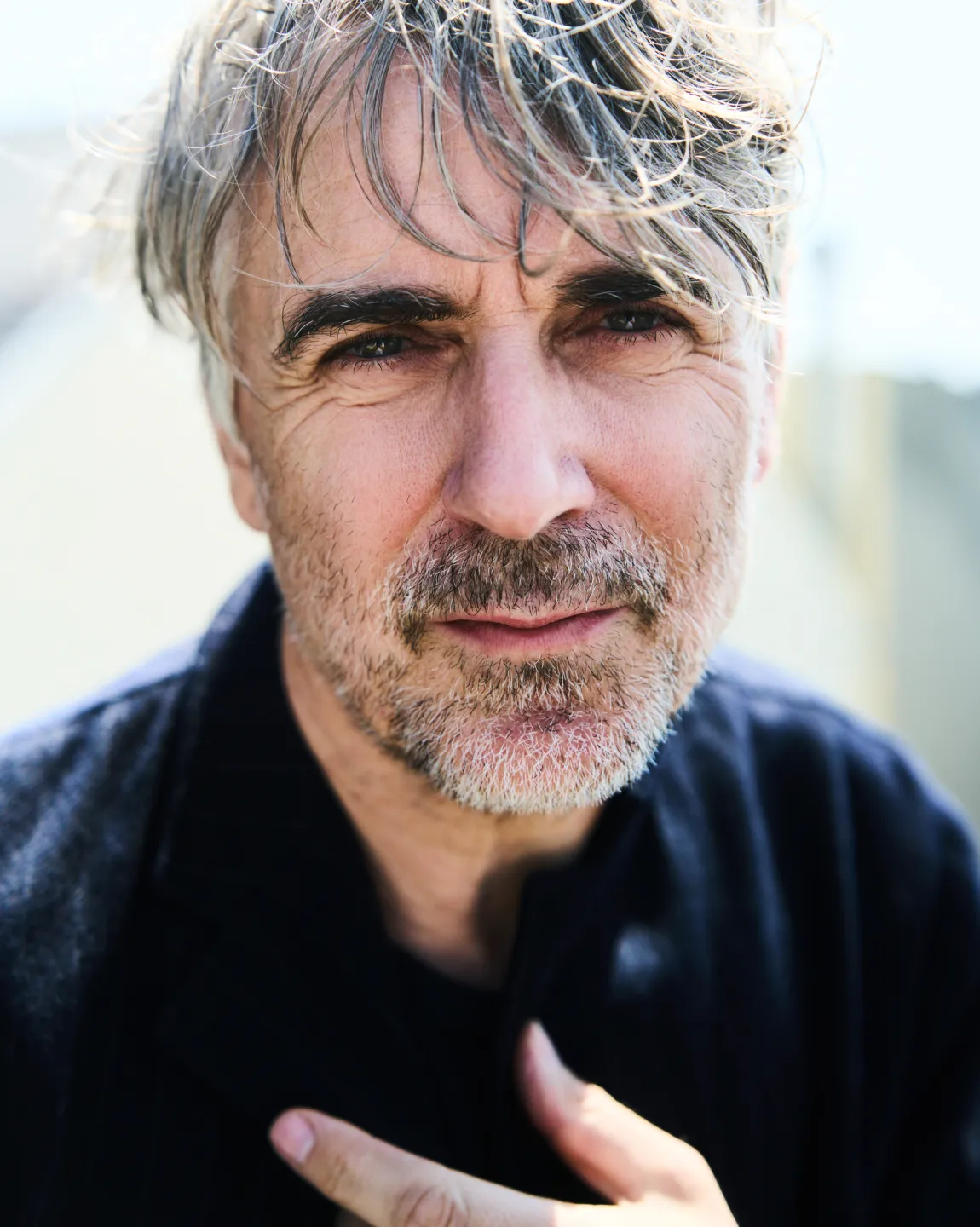 Schauspieler Jens Harzer im Profil, er schaut in die Kamera, hat eine Hand an der Brust.