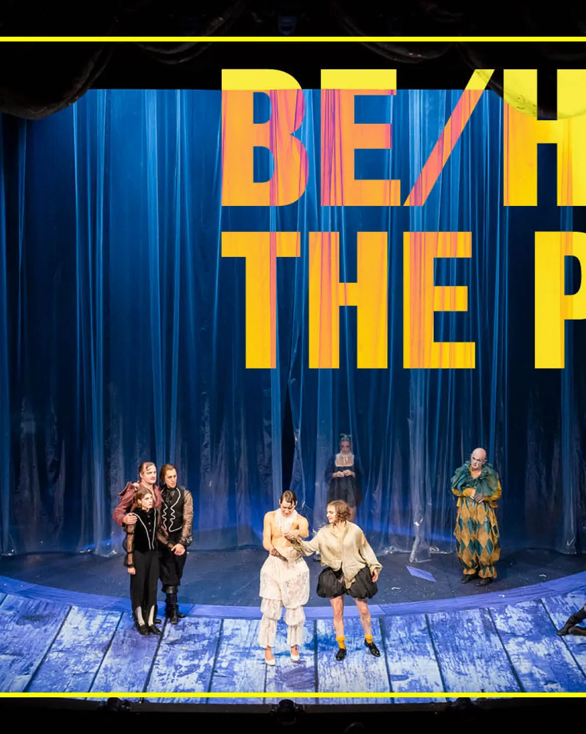 Ein Foto vom Bühnenportal, blaues Licht, vor einem beleuchteten Plastikvorhang sind einige Figuren in aufwändigen Kostümen zu erkennen. 