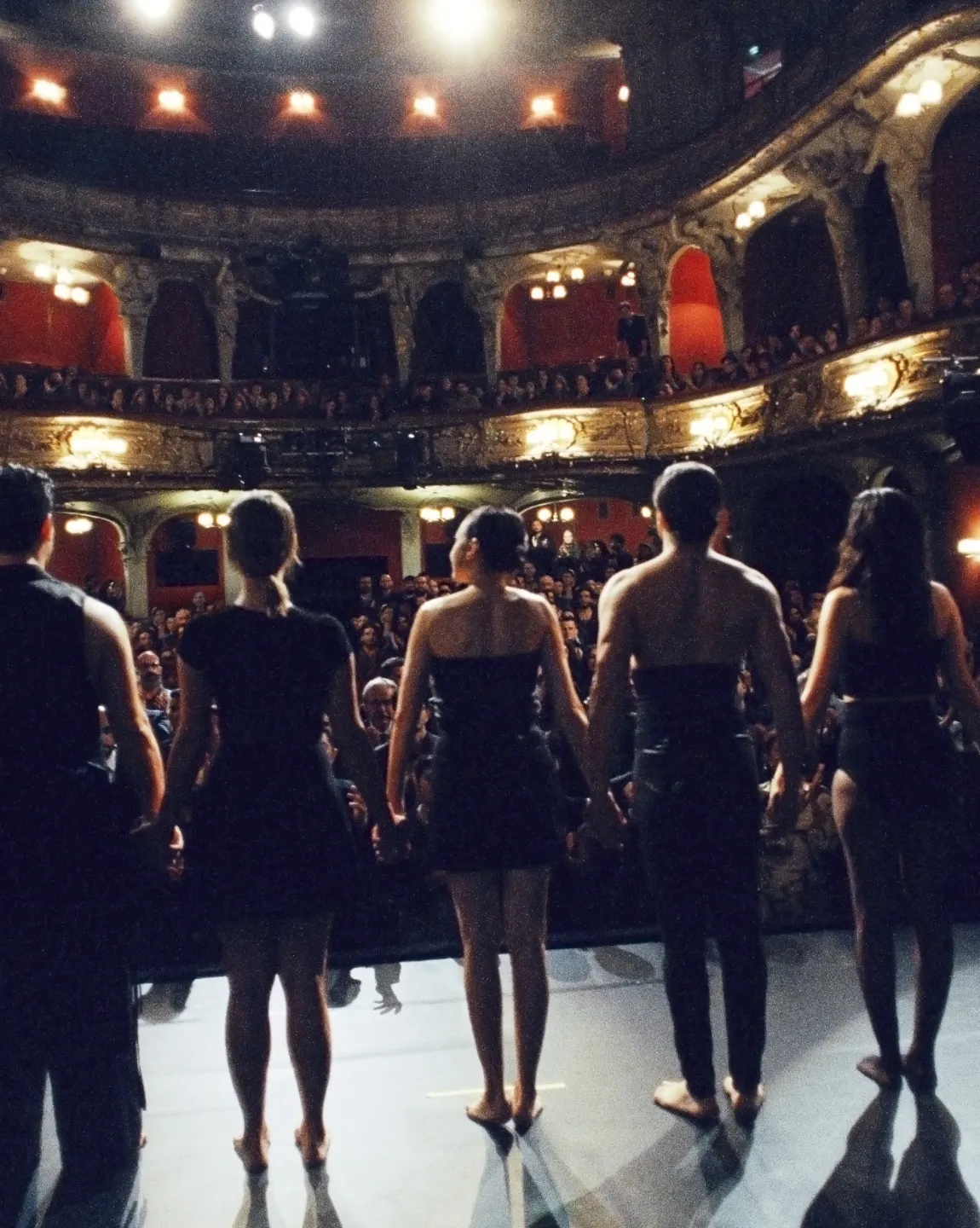 Blick von der BE-Bühne in den Zuschauerraum. An der Rampe stehen acht Tänzer:innen, denen applaudiert wird. 