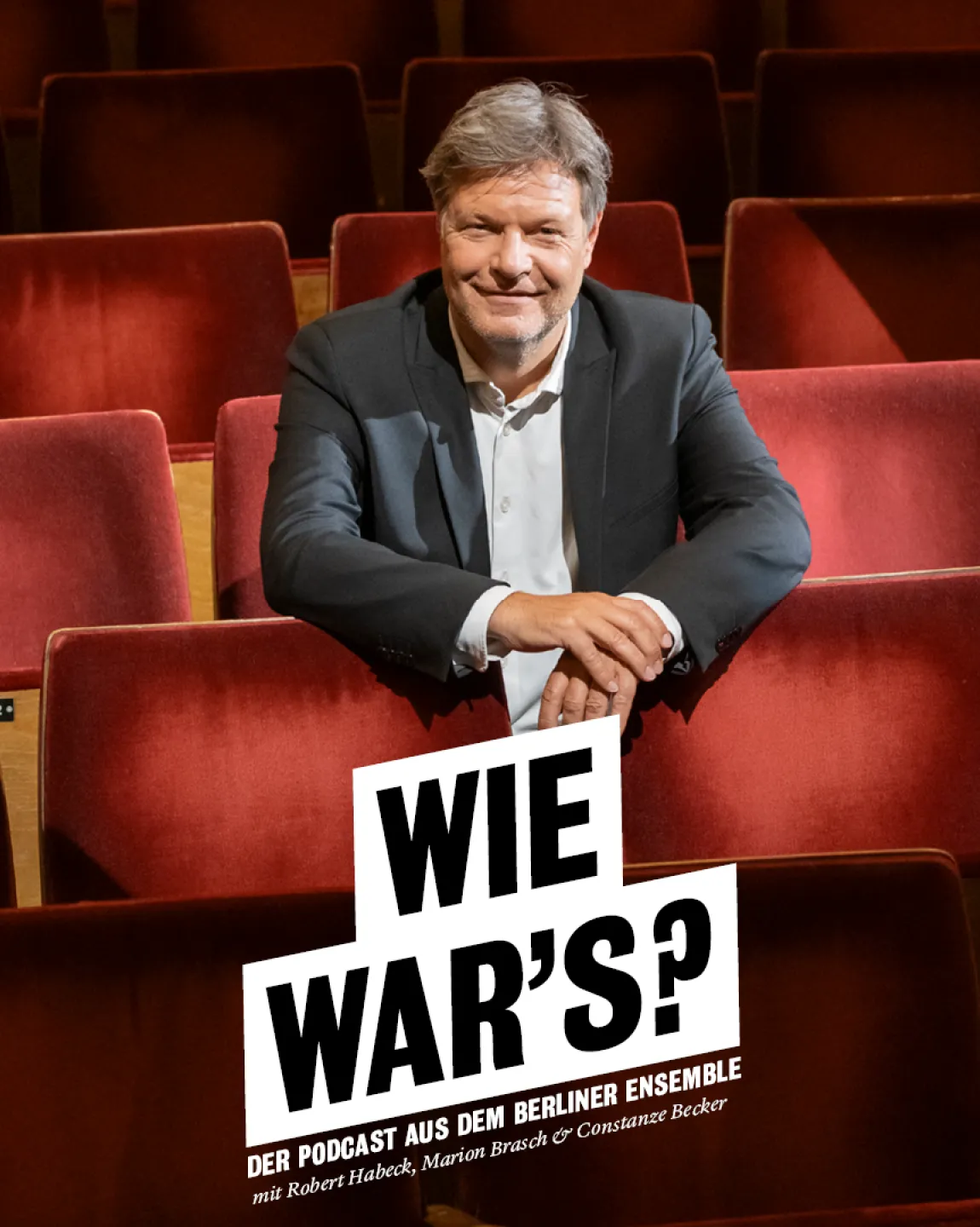 Robert Habeck sitzt im Zuschauerraum des Großen Hauses, was an den samtigen Sitzen zu erkennen ist. Die Arme hat er auf die Vordersitze gestützt, er lächelt direkt in die Kamera.
