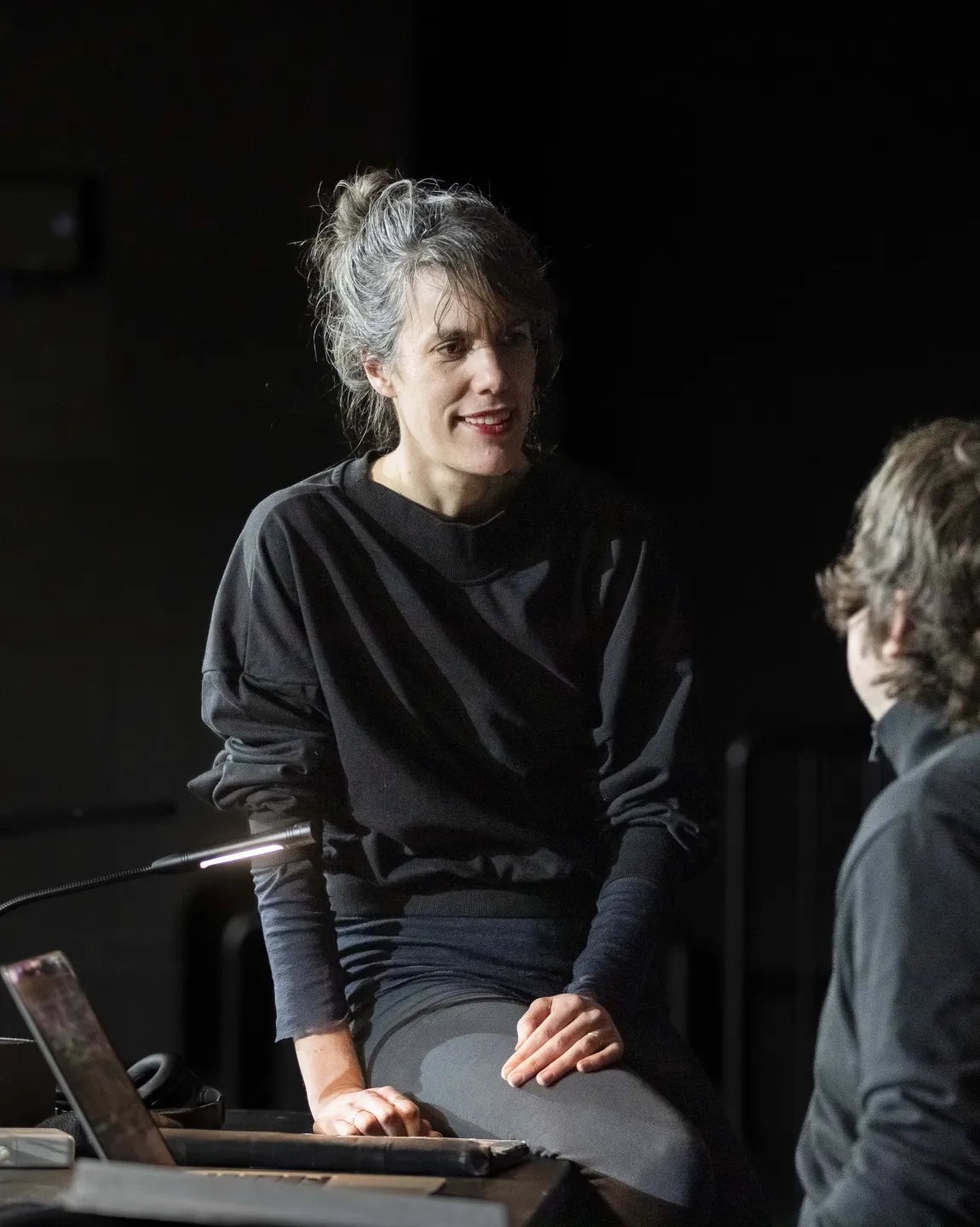 Person in schwarzer Kleidung sitzt auf einem Tisch und unterhält sich mit einer anderen Person