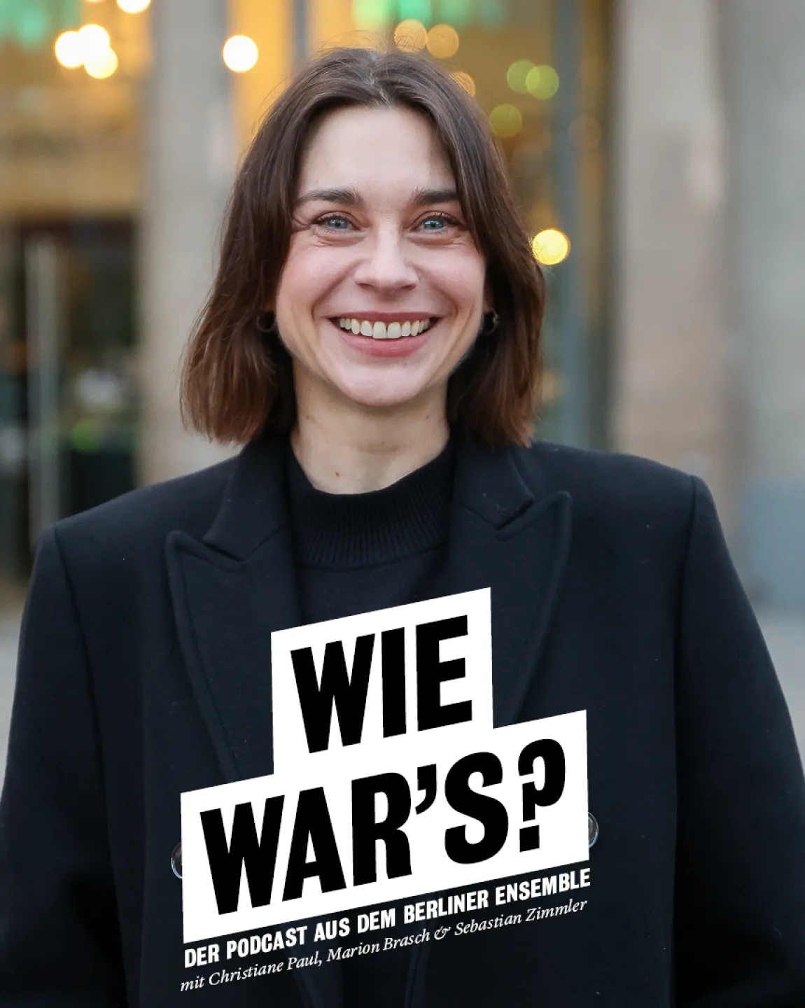 Portrait von Christiane Paul vor dem Berliner Ensemble, im Hintergrund ist der Shop zu erkennen. Sie trägt einen dunklen Mantel und lacht offen in die Kamera. 