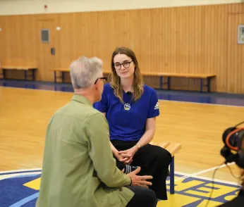 Oliver Reese und Wiebke Schwartau sitzen in der Mitte der Sporthalle, es ist Reeses Rücken zu sehen und Schwartau frontal. 
