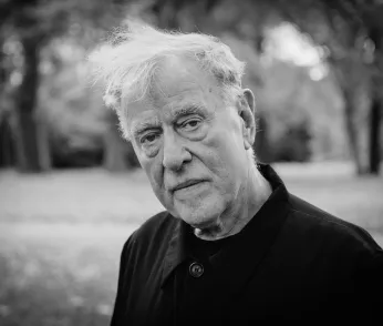 Ein schwarzweisses Protrait von Claus Peymann, er trägt ein dunkles Oberteil und neigt den Kopf. 