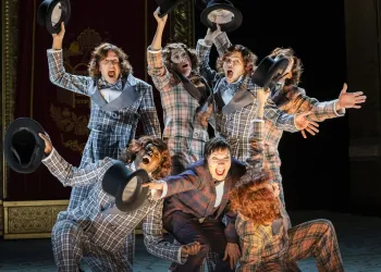 24)	Sieben Personen in karierten Anzügen stehen eng zusammen und strecken schwarze Zylinderhüte in die Luft.