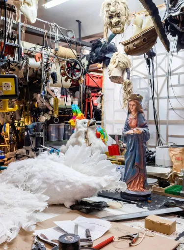 Werkstatt mit großer Werkbank und vielen Geräten und Maschinen, im Vordergrund Tisch mit einer künstlichen Gans und einer Madonnenfigur