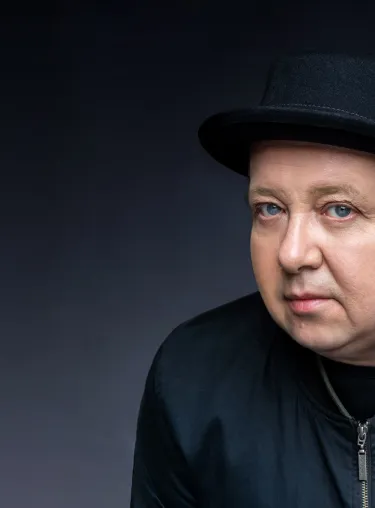 Musiker und Autor Sebastian Krumbiegel im Halbprofil mit Hut und dunkler Jacke vor dunklem Studiohintergrund