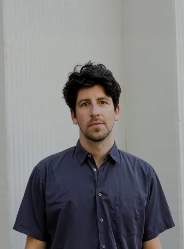 Lucien Strauch in blauem Hemd-Shirt vor weißer Wand