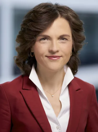 Portrait-Aufnahme von Elisabeth Kaiser in weißem Hemd und rotem Sakko, der Hintergrund ist unscharf.