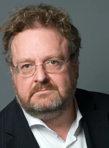 Jürgen Kaube in Anzug und Hemd vor grauer Wand, blickt in die Kamera.