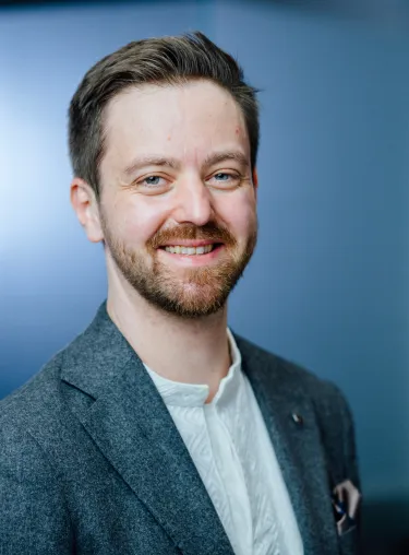 Mattia Nelles vor blauer Wand, schaut in die Kamera.