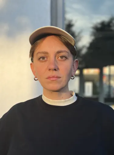 Olivia Schneider in schwarzem Pullover und beiger Cap, blickt in die Kamera, der Hintergrund ist unscharf.