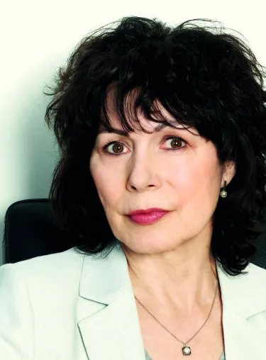 Sabine Adler in weißem Blazer vor weißer Wand. 