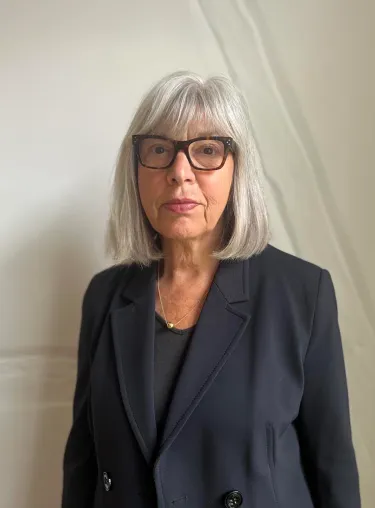 Rebecca Harms in dunklem Blazer vor heller Wand. Sie trägt Brille und schaut in die Kamera.