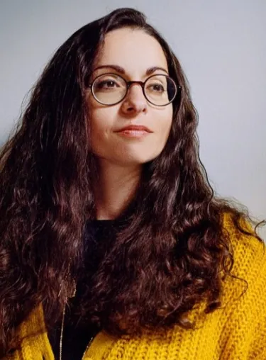 Porträt von Marina Chernivsky mit gelber Weste vor einer weißen Wand