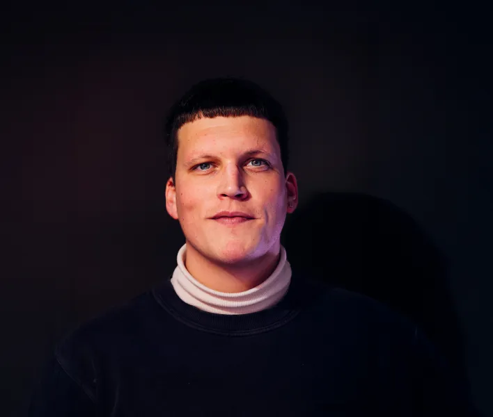 Potraitaufnahme von August Modersohn in schwarzem Oberteil mit weißem Kragen vor schwarzem Hintergrund, er lächelt und schaut in die Kamera.