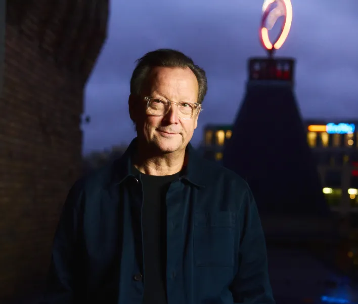 Matthias Brandt steht im Dunkeln auf dem Dach des Berliner Ensembles, im Hintergrund ist das leuchtende Logo zu erkennen.